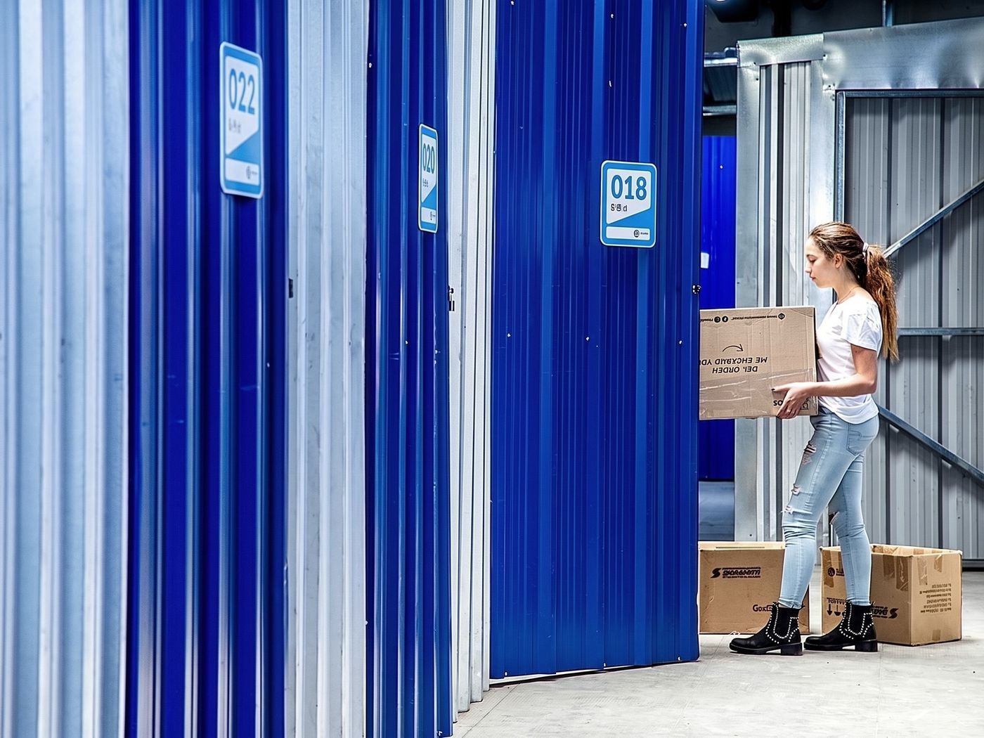 Clienta con una caja frente a las bauleras de puerta azul de +Metros Almagro
